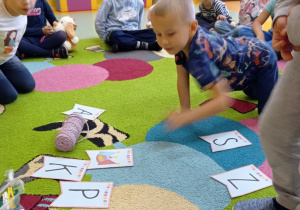 chłopiec z dziewczynką oglądają rozsypankę literową na dywanie dzieci w tle grzecznie siedzą na dywanie